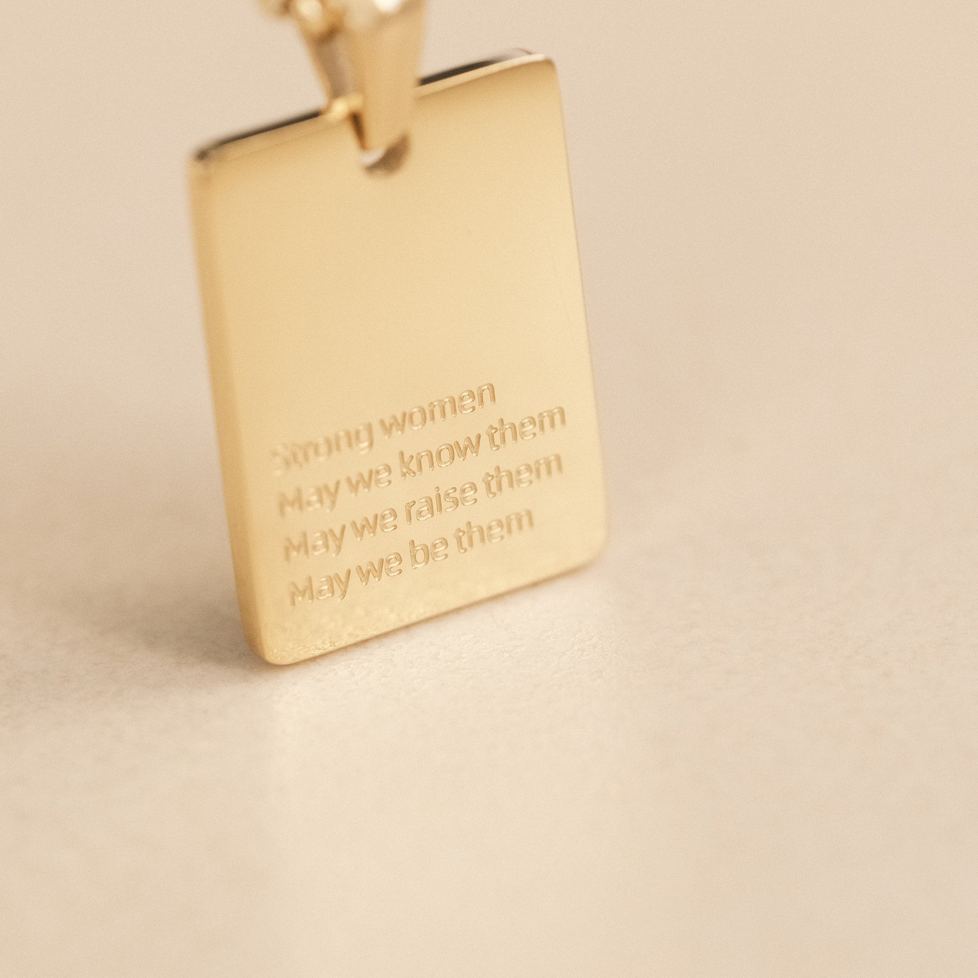 a gold square pendant with a chain on a table