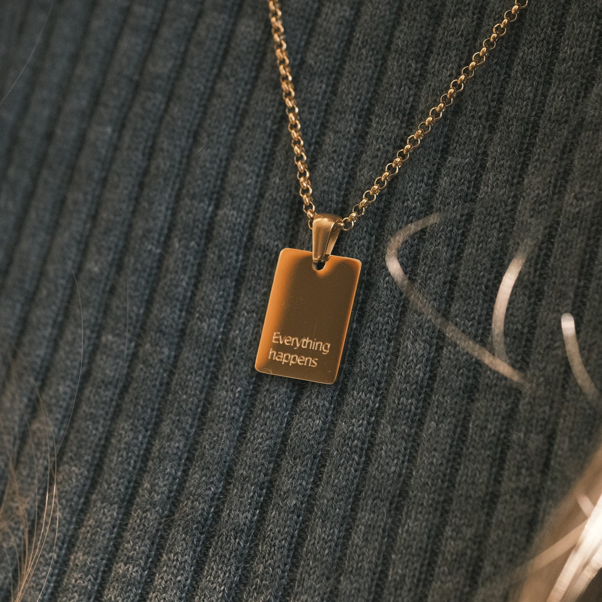 a gold necklace with a square tag on it